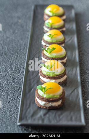 Canape with cream cheese, guacamole and fried quail eggs on the plate Stock Photo