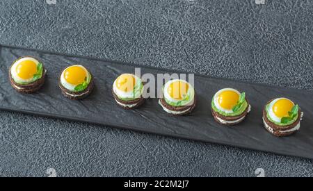 Canape with cream cheese, guacamole and fried quail eggs on the plate Stock Photo