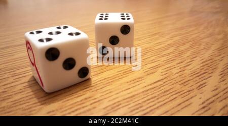 Two white playing dice with black numbers on a light wooden table. Stock Photo