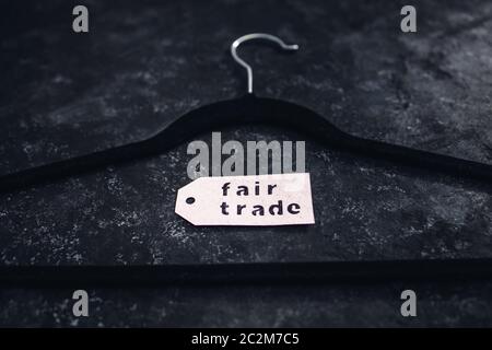 ethical fashion concept, velvet clothes hanger with Fair Trade label on it on black background Stock Photo