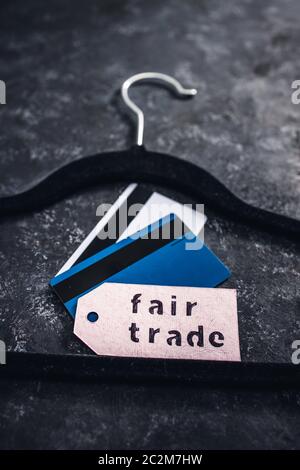 ethical fashion concept, velvet clothes hanger with Fair Trade label and credit cards on it on black background Stock Photo