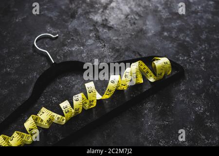 fashion industry and risks of eating disorders concept, velvet hanger with yellow measuring tape on it on black background Stock Photo