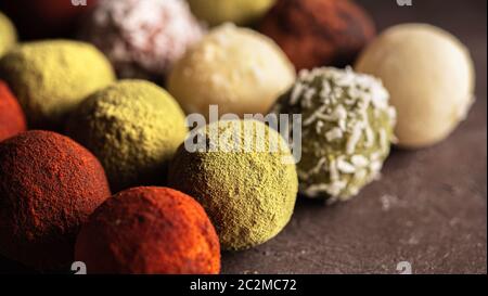 Colorful homemade truffles coated in dry beet powder, matcha tea powder, shredded cococnut on dark background. Copy space for text or design, banner. Stock Photo