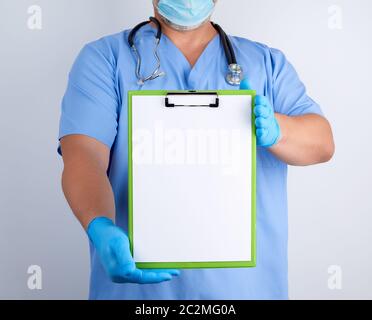 doctor in blue uniform and latex gloves holds a green holder for sheets of paper, empty space for writing text, white background Stock Photo