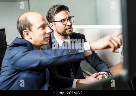 Image of two thoughtful businessmen looking at data on multiple computer screens, solving business issue at business meeting in modern corporate offic Stock Photo