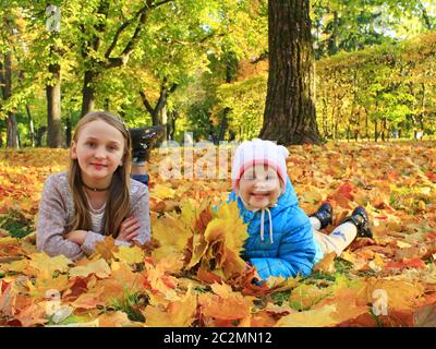 Adorable little kids playing in autumn park. Young sisters laying on bright yellow and orange leaves Stock Photo
