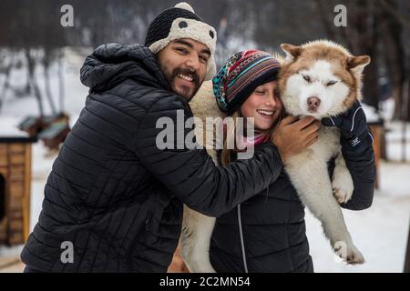 couple carrying a siberian dog in winter surrounded by snow. Stock Photo