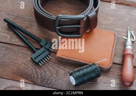 Brown leather belt, wallet and leather crafting tools on wooden desk Stock Photo