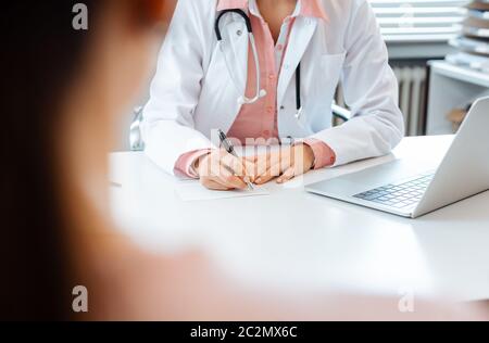 Close-up of doctor taking notes while having appointment with woman patient Stock Photo