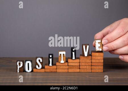 POSITIVE. Growth, motivation and inspiration concept. Wooden alphabet letters on steps. Gray background Stock Photo