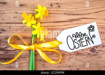 Label With German Calligraphy Frohe Ostern Means Happy Easter. Yellow Spring Narcissus Flower On Rustic Wooden Background. Stock Photo