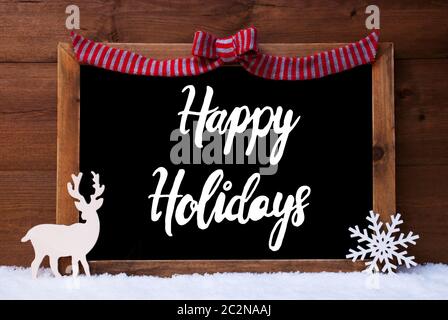 Chalkboard With English Calligraphy Happy Holidays. Christmas Decoration Like Deer And Bow. Wooden Background With Snow Stock Photo