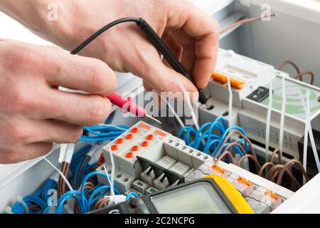 Hands of an electrician with multimeter probe at an electrical switchgear cabinet Stock Photo