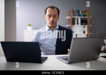 Businessperson Doing Multitasking Work On Two Laptops At Workplace Stock Photo