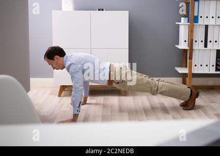 Side View Of A Young Businessman Doing Push Up In Office Stock Photo