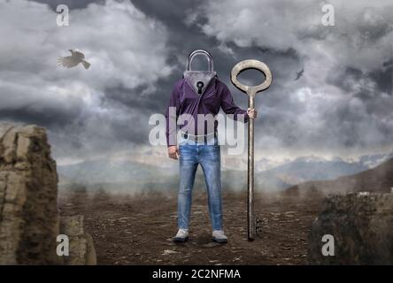 Man with keyhole instead of a head holds large key, dry desert on background. Hard way to freedom concept Stock Photo