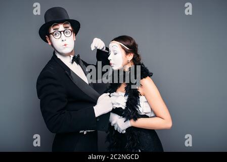 Mime artists with white makeup masks on faces. Pantomime theater actor and actress performing against black background. Comedy performers Stock Photo