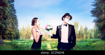 Mime actor and actress performing with flower bouquet, green nature on background. Pantomime theater performers posing. Comedy artists Stock Photo