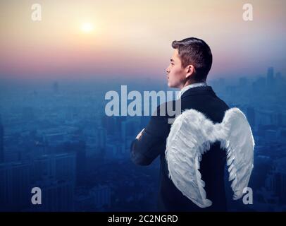 Businessman with angel wings on his back looking at sunrise over city Stock Photo