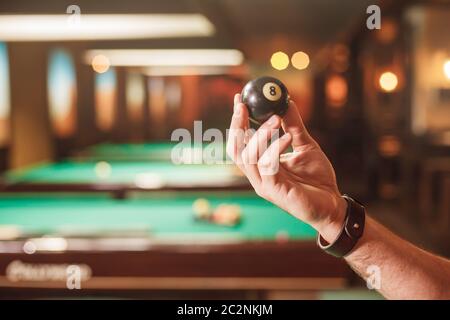 The male hand shows a billiard sphere number eight. Billiard tables on the background. Stock Photo