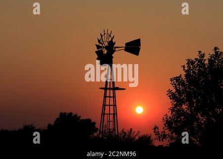 Kansas Windmill Silhouette with a bright Orange Sunset and tree Silhouettes. Stock Photo