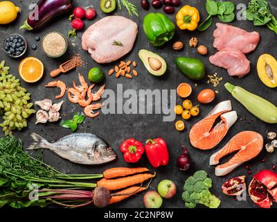 Pegan diet conept with copy space in center. Vegan plus paleo diet food ingredients - vegetables, fruits, raw meat and fish on dark background. Top vi Stock Photo