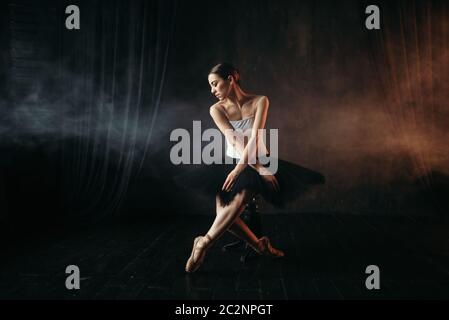 Ballet dancer sitting on black banquette on the stage in theatre. Graceful ballerina training in class Stock Photo