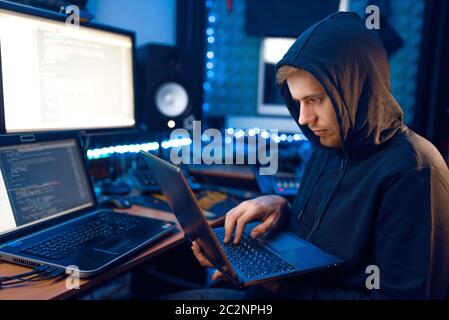 Hacker in hood shows thumbs up at his workplace with laptop and PC, password or account hacking. Internet spy, crime lifestyle Stock Photo