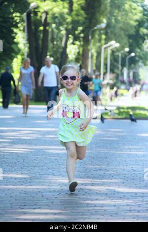 Happy little girl running in city park. Positive childish emitions. Child running along path smiling Stock Photo