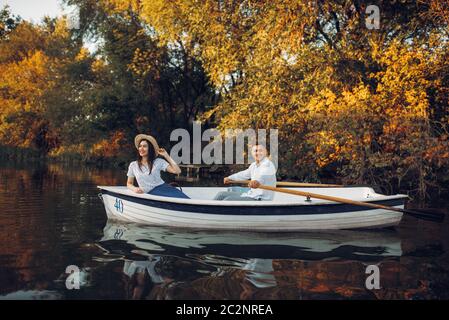 Love couple in boat on quiet lake at summer day, daydream, side view. Romantic date, boating trip, man and woman walking along the river Stock Photo