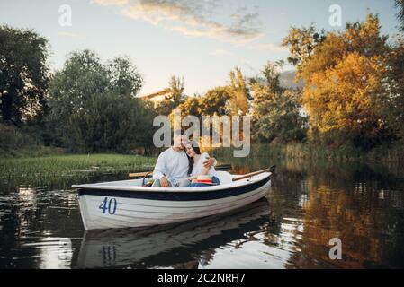 Love couple hugs in a boat on quiet lake at summer day. Romantic meeting, boating trip, man and woman walking along the river Stock Photo