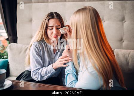 Young woman calms her girlfriend in cafe. Female friends leisures in restaurant, gossipers meeting Stock Photo