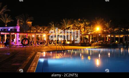 Swimming pool and night hotel on holidays. People relax in evening near pool. Lights of evening hote Stock Photo