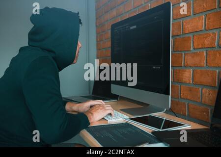 Hacker in the hood working with computer with hacking breaking into data servers. Stock Photo