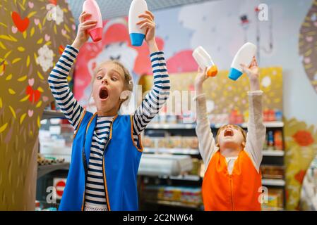 Little girls in uniform playing with shampoo, playroom. Kids plays sellers in imaginary supermarket, salesman profession learning, children on playgro Stock Photo