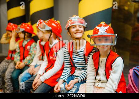 Children in helmets and uniform playing fireman, playroom indoor. Kids lerning firefighter profession. Boys and girls plays lifeguards, little heroes Stock Photo