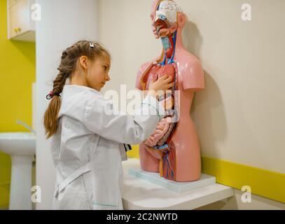 Cute girl in uniform and with stethoscope playing doctor, playroom. Kid plays medicine worker in imaginary hospital, profession learning at the medica Stock Photo