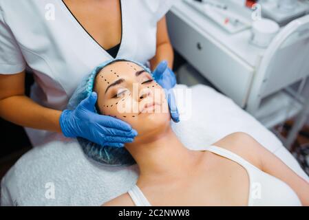 Cosmetician makes botox injection in dotted lines on female patient face, botox injections preparation. Rejuvenation procedure in beautician salon. Co Stock Photo