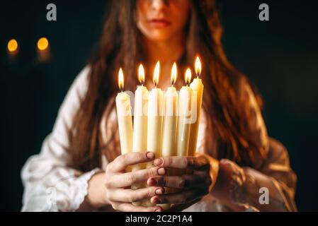 Female person in white shirt holds candles in hands. Dark magic ritual, occultism and exorcism, divination Stock Photo