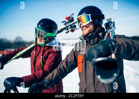 Male and female skiers poses with skis and poles in hands, blue sky and snowy mountains on background. Winter active sport, extreme lifestyle. Downhil Stock Photo