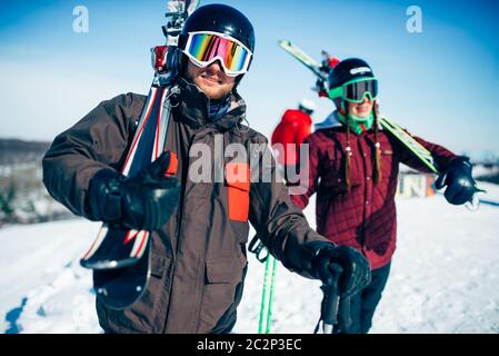 Male and female skiers poses with skis and poles in hands, blue sky and snowy mountains on background. Winter active sport, extreme lifestyle. Downhil Stock Photo