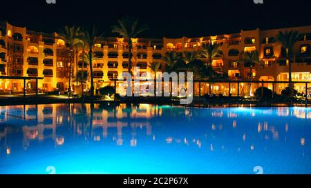 Lights of evening hotel are reflected in pool water in night. Bright lights of resort hotel in Hurgh Stock Photo