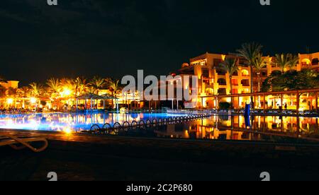Lights of evening hotel are reflected in pool water in night. Bright lights of resort hotel Stock Photo