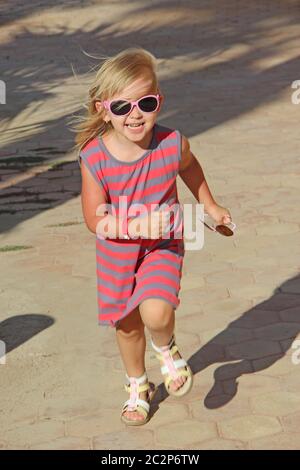 Happy little girl running in city park. Positive childish emotions. Child running along path smiling Stock Photo