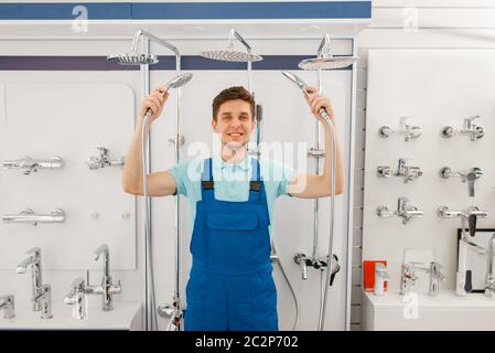 Plumber in uniform choosing shower at showcase in plumbering store. Man buying sanitary engineering in shop, bathroom equipment choice Stock Photo