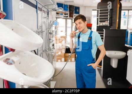 Plumber in uniform buying shower at showcase in plumbering store. Man buying sanitary engineering in shop, bathroom equipment choice Stock Photo