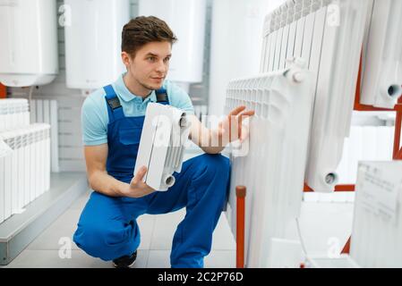Plumber in uniform shows water heating radiator in plumbering store. Man buying sanitary engineering in shop Stock Photo