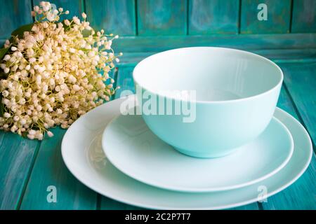 table setting with bouquet of lilies of the valley, empty dishes in teal color Stock Photo