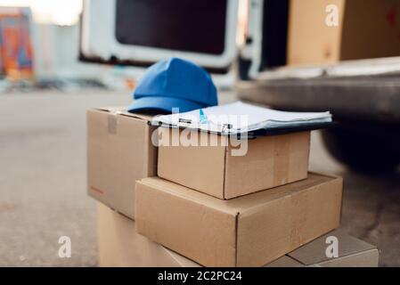 Parcel boxes and cap with notebook, delivery service concept, delivering business, nobody. Cardboard packages, deliver, courier or shipping job Stock Photo