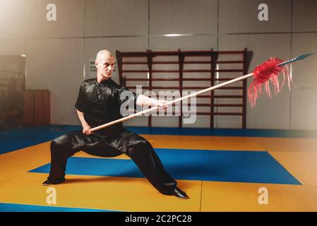 Wushu master training with spear, martial arts. Man in black cloth poses with blade Stock Photo